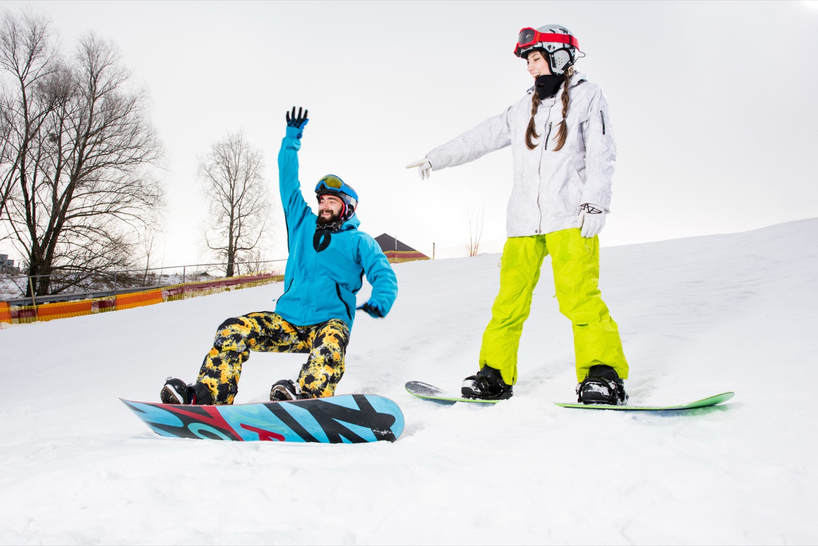 Snowboard coach guiding a beginner sitting on their board, both wearing helmets