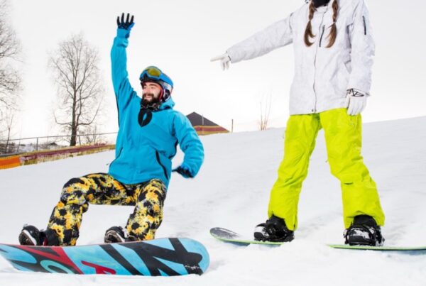Snowboard coach guiding a beginner, both wearing helmets