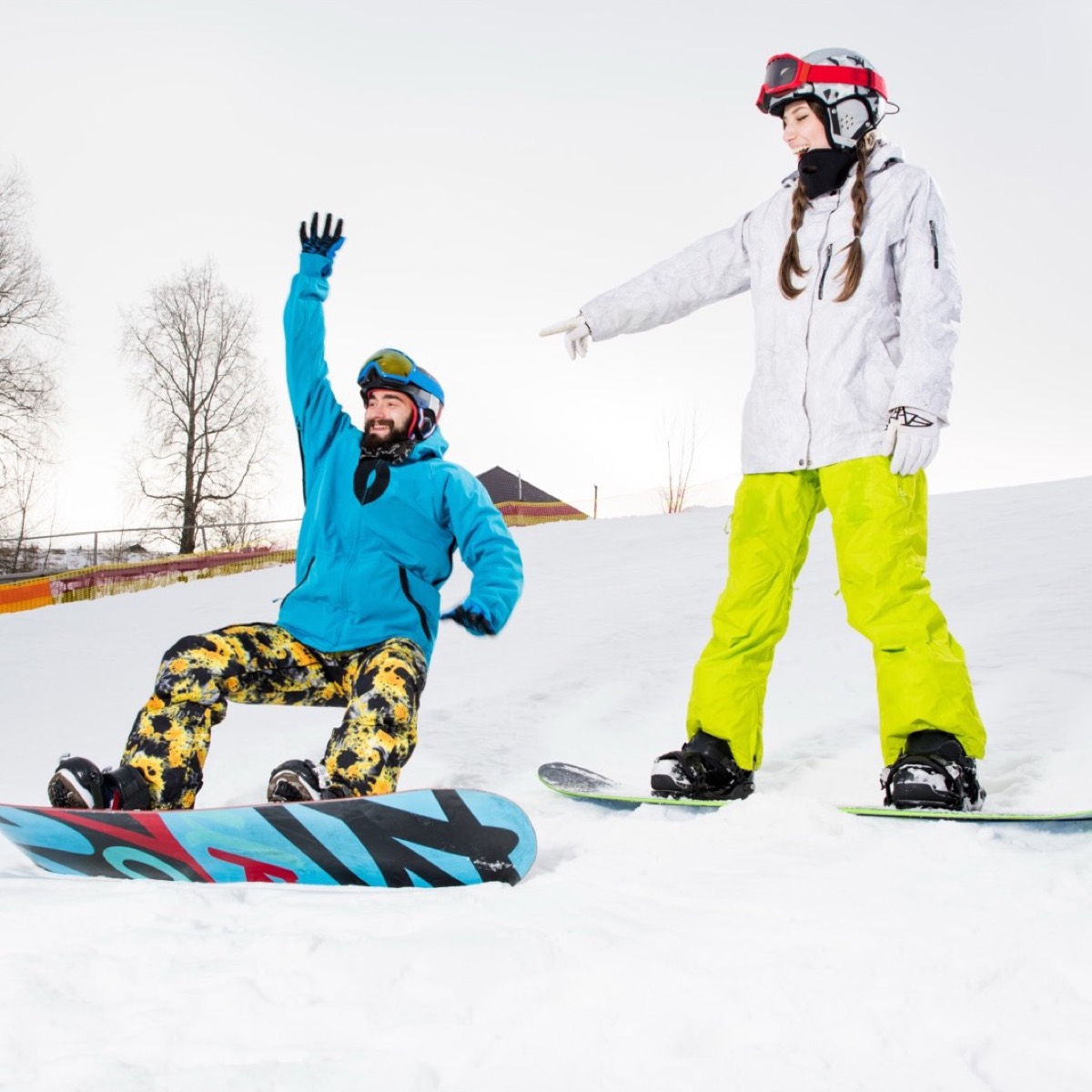 Snowboard coach guiding a beginner, both wearing helmets