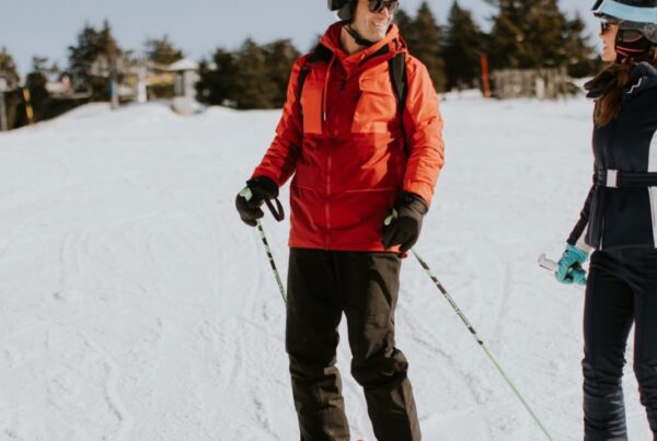 Ski coach and guest talking on a groomed run, both wearing helmets