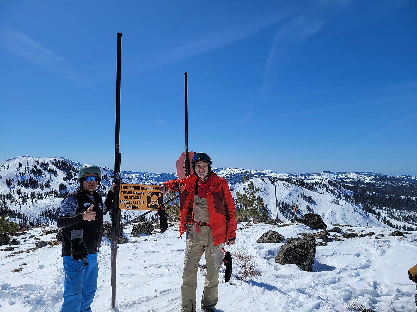Coach Jason in uniform on the mountain with a guest, both wearing helmets