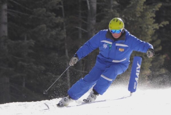 Coach Jon carving past a race gate in ski school uniform and helmet