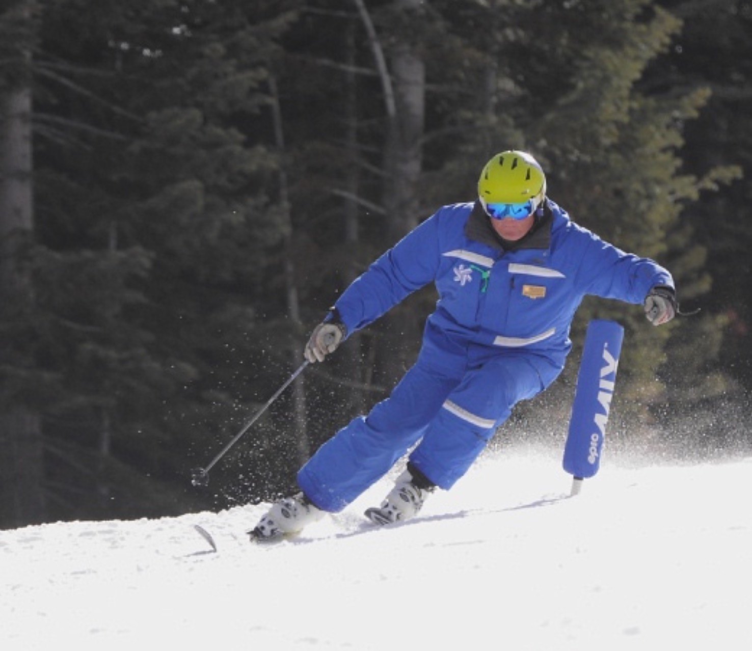 Coach Jon carving past a race gate in ski school uniform and helmet