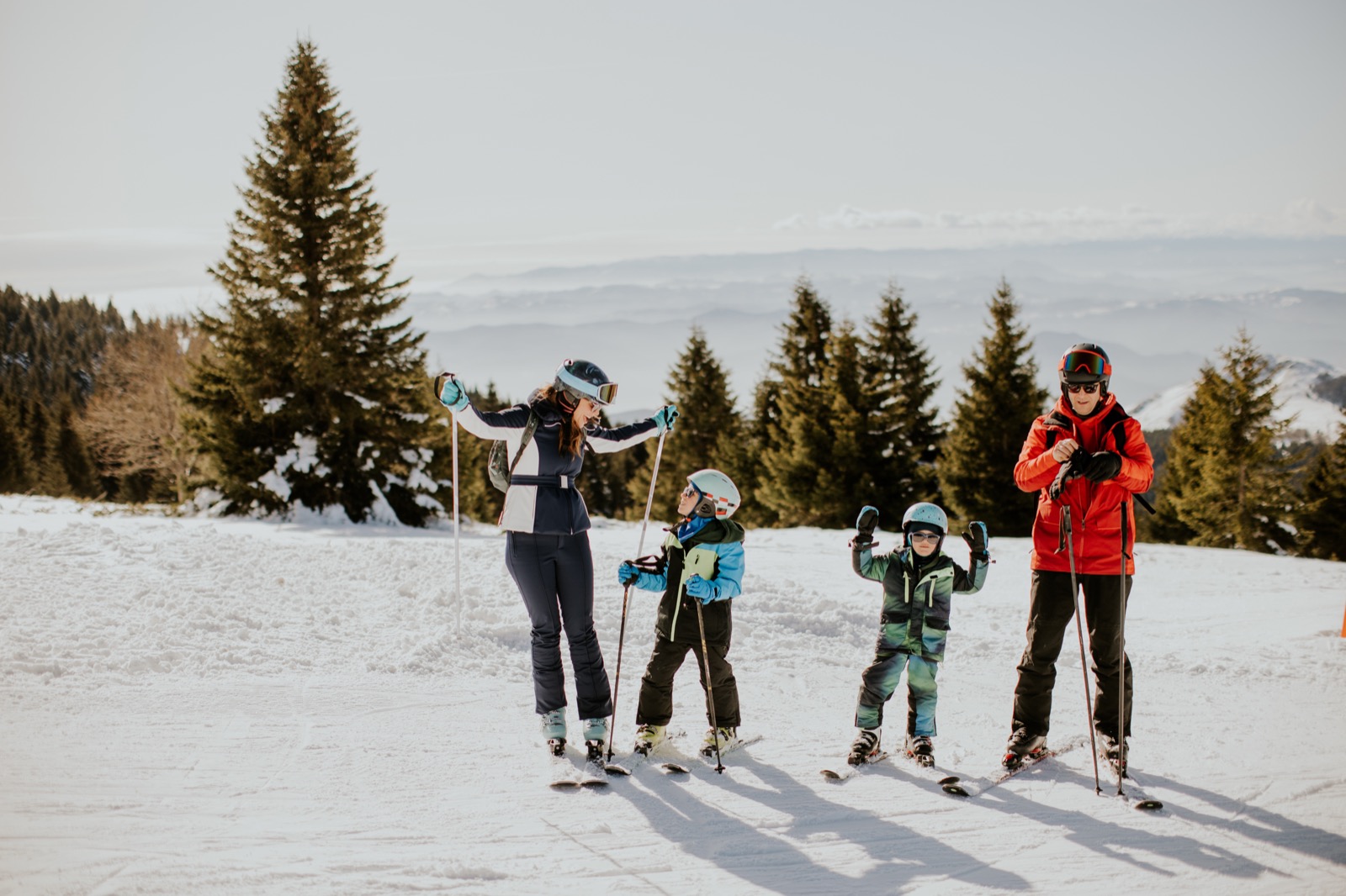 Two adults and two children, all wearing helmets, on a groomed run at a ski resort