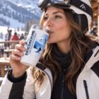 A skier in a helmet drinking from a SkiCoach.Me 20oz insulated tumbler